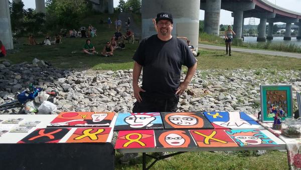 Jason Weingberg standing at a table with Flask hate on displaying his artwork.